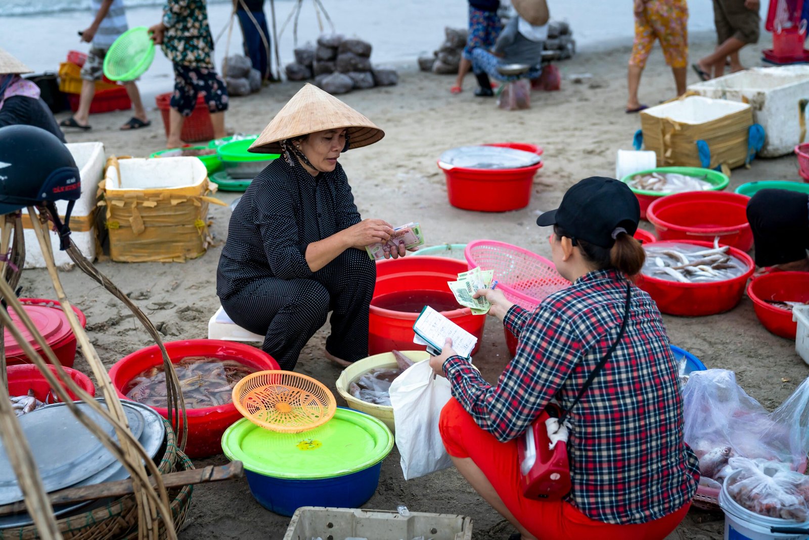 Lively beachside fish market with vendors and buyers engaged in seafood transactions.